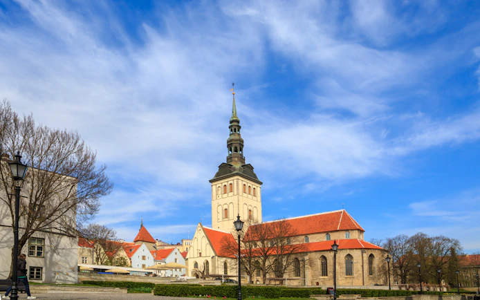 St. Nicholas' Church with its tall spire in Tallinn, Estonia, under a blue sky.
