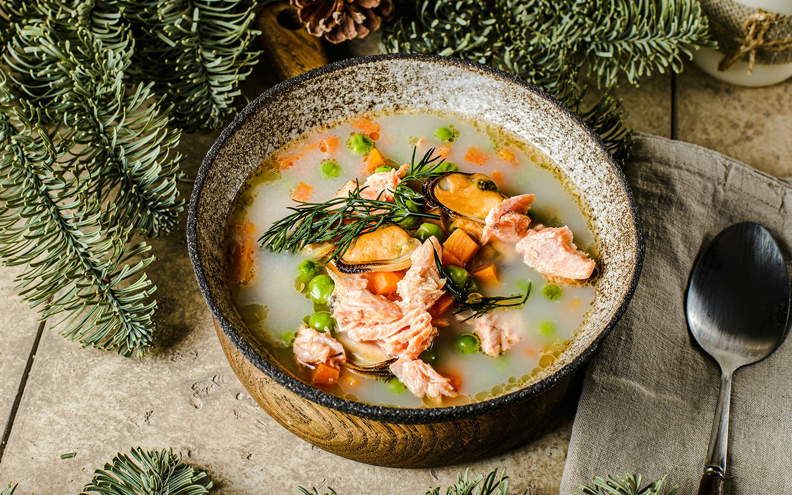 Salmon fish soup with mussels, peas, and carrots in a rustic bowl, garnished with herbs.