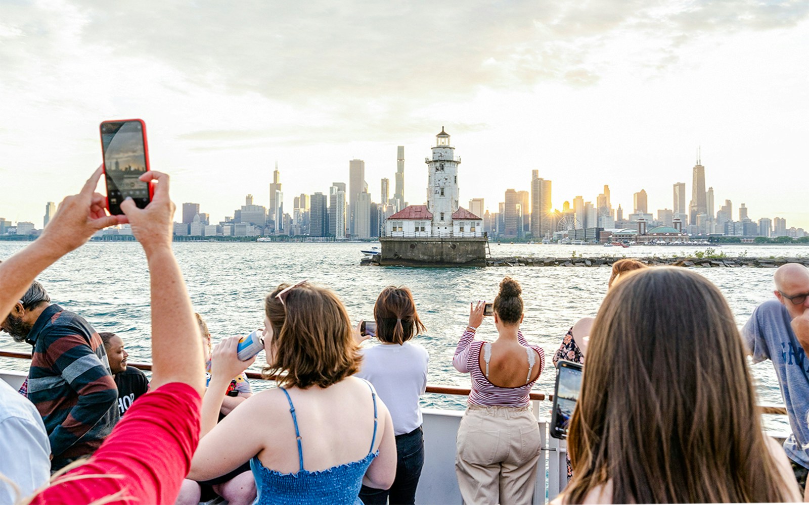 People enjoying a sunset cruise on Lake Michigan with a view of a lighthouse and Chicago skyline.