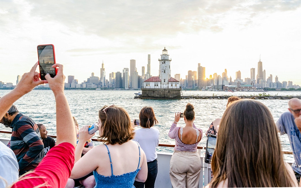 People enjoying a sunset cruise on Lake Michigan with a view of a lighthouse and Chicago skyline.