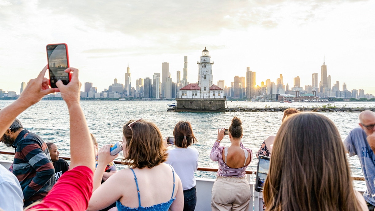People enjoying a sunset cruise on Lake Michigan with a view of a lighthouse and Chicago skyline.