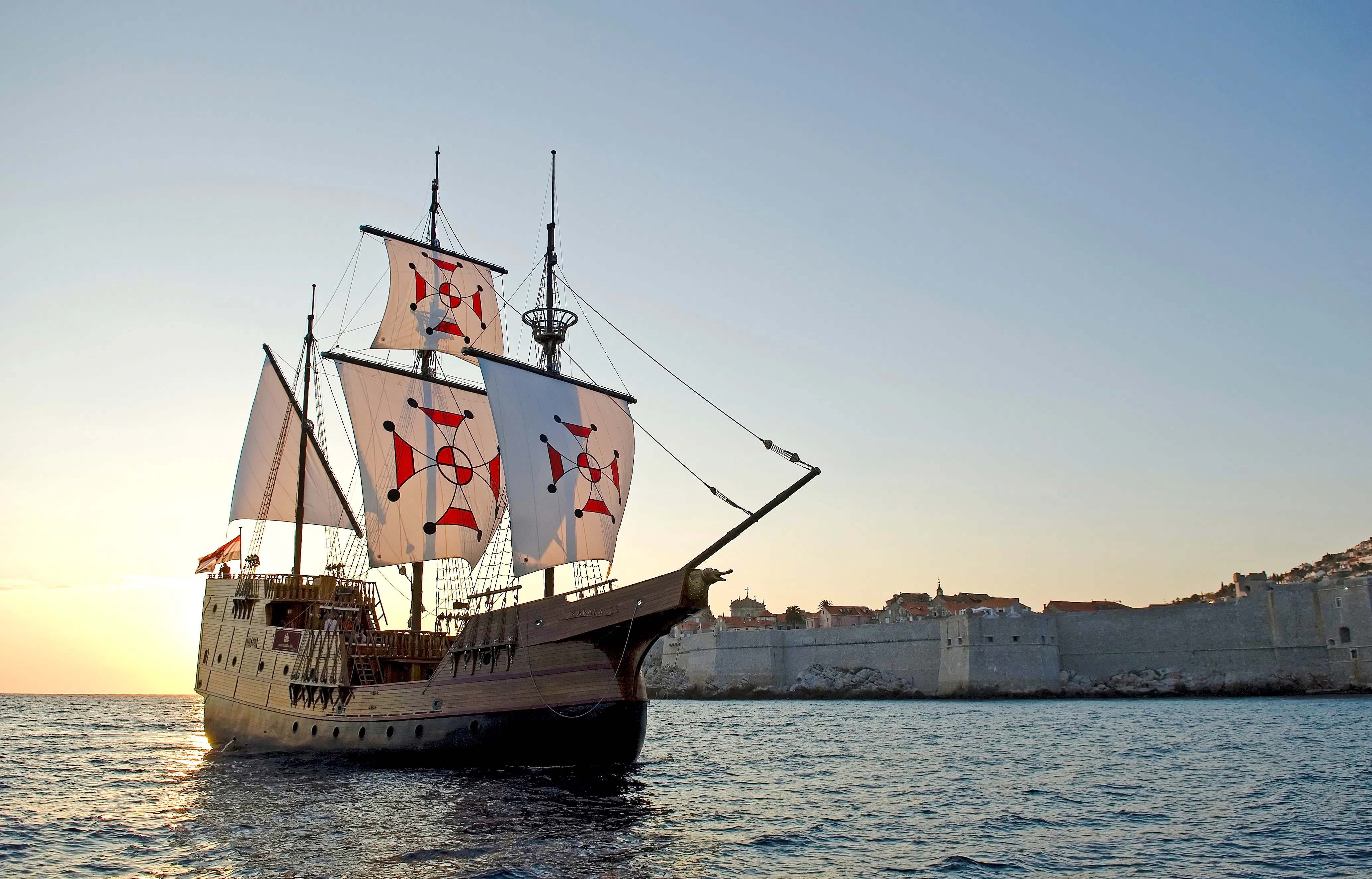 Pirate ship sailing near Dubrovnik Old Town at sunset.
