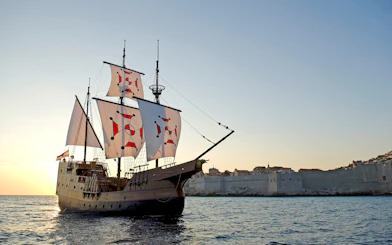 Pirate ship sailing near Dubrovnik Old Town at sunset.