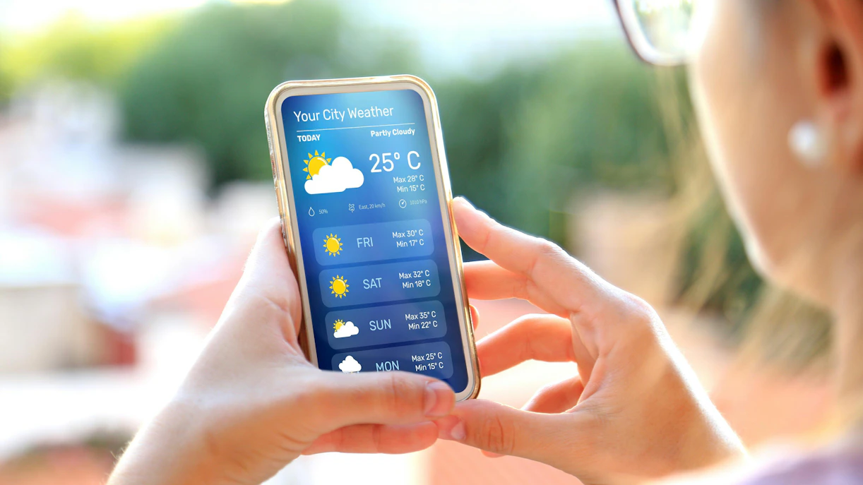 Woman checking weather forecast on smartphone outdoors in Queenstown before skydiving adventure.