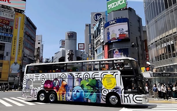 Colorful tour bus in Shibuya, Tokyo, with vibrant street art and cityscape background.