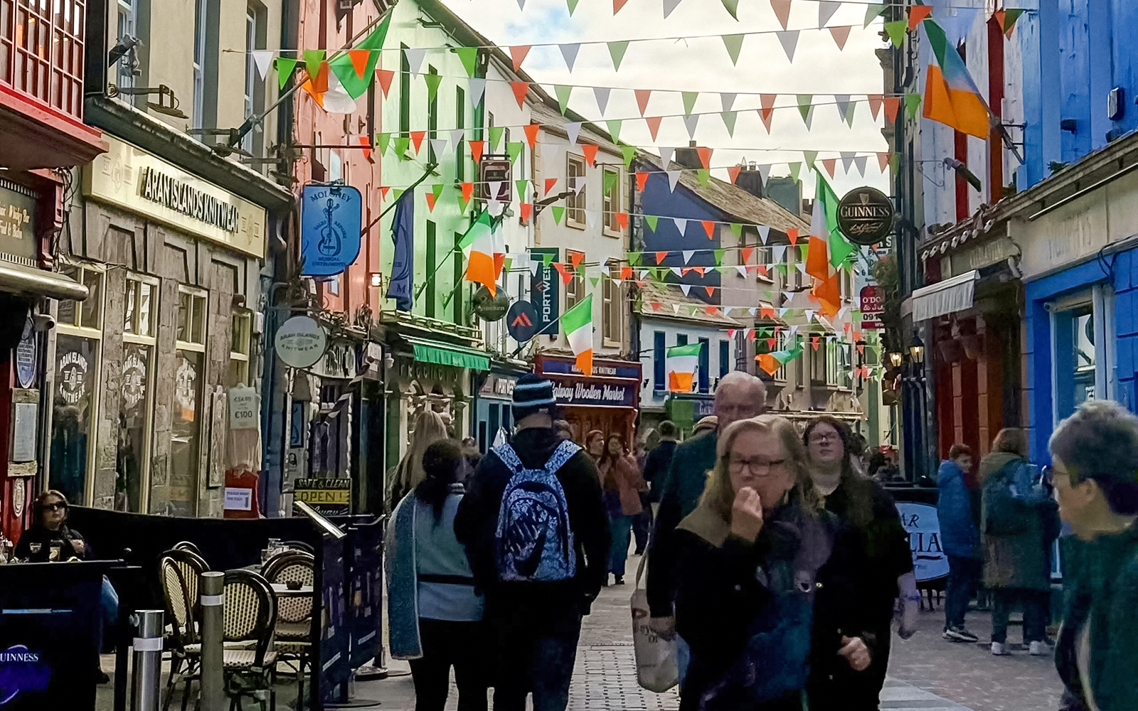 Colorful street in Galway City with people walking and Irish flags hanging above.