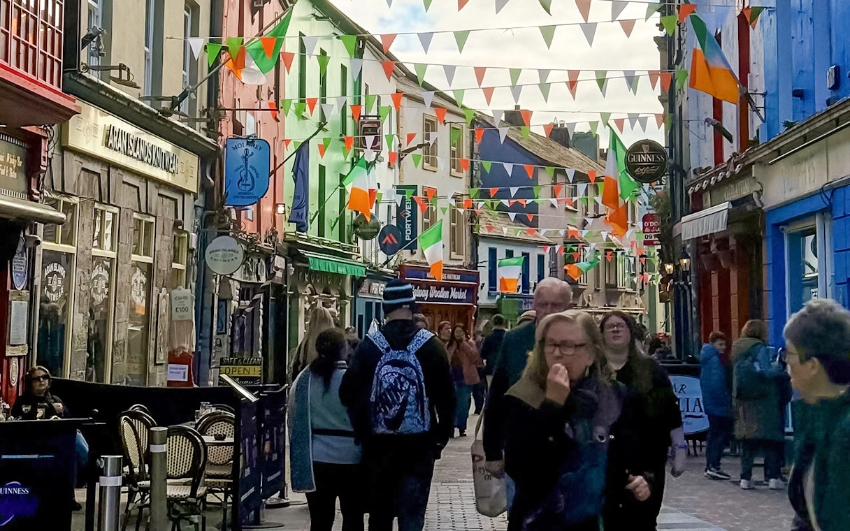 Colorful street in Galway City with people walking and Irish flags hanging above.
