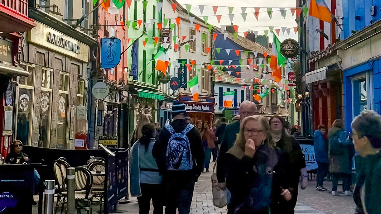 Colorful street in Galway City with people walking and Irish flags hanging above.