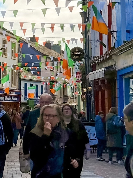 Colorful street in Galway City with people walking and Irish flags hanging above.