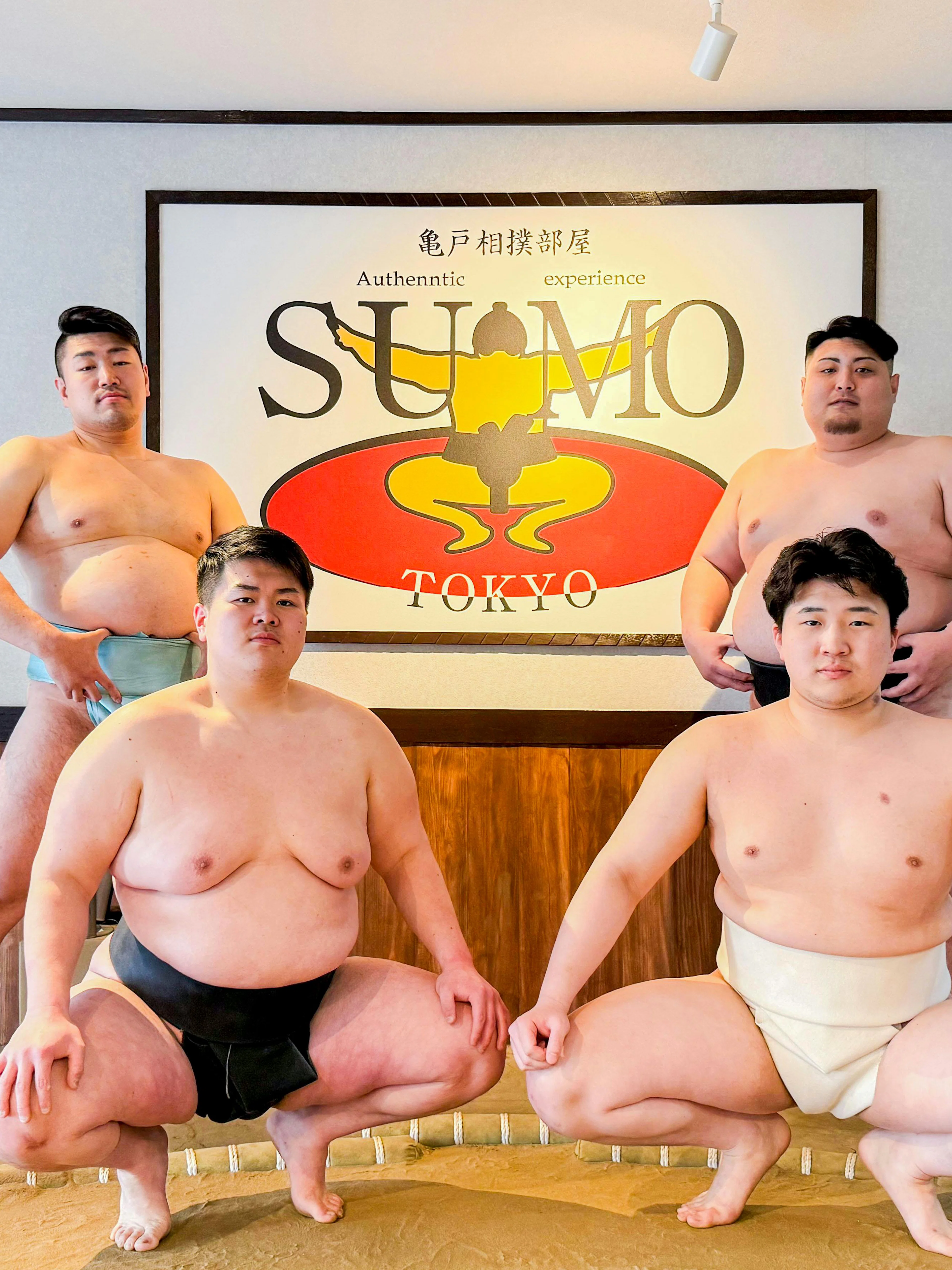 Sumo wrestlers posing in front of a Tokyo sign at an authentic sumo experience.