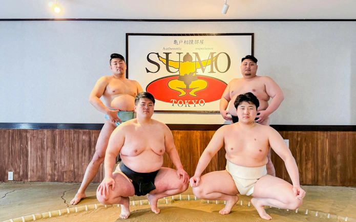 Sumo wrestlers posing in front of a Tokyo sign at an authentic sumo experience.