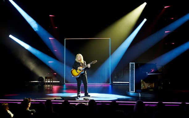 Musician performing on stage with guitar under spotlight during "Melissa Etheridge: My Window" show.