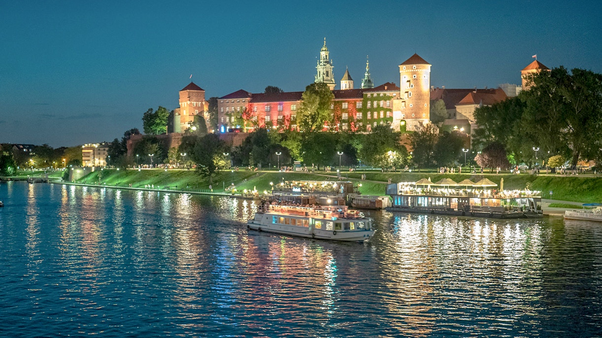 Cruise boat on Vistula River with Wawel Castle illuminated at night in Krakow.