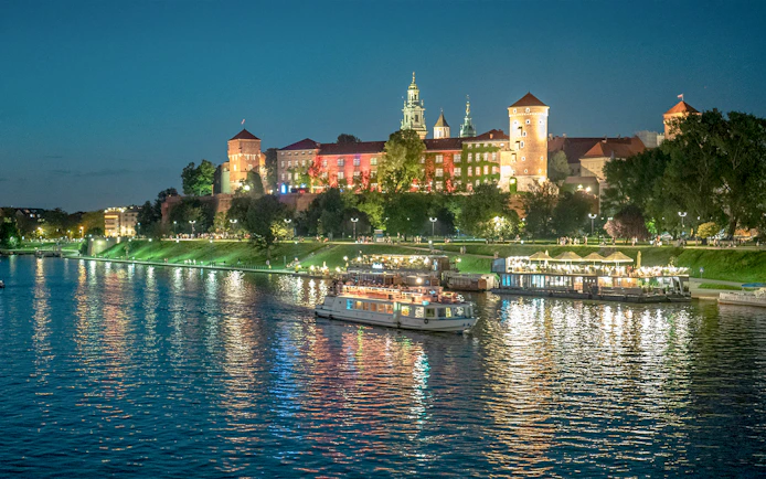 Cruise boat on Vistula River with Wawel Castle illuminated at night in Krakow.