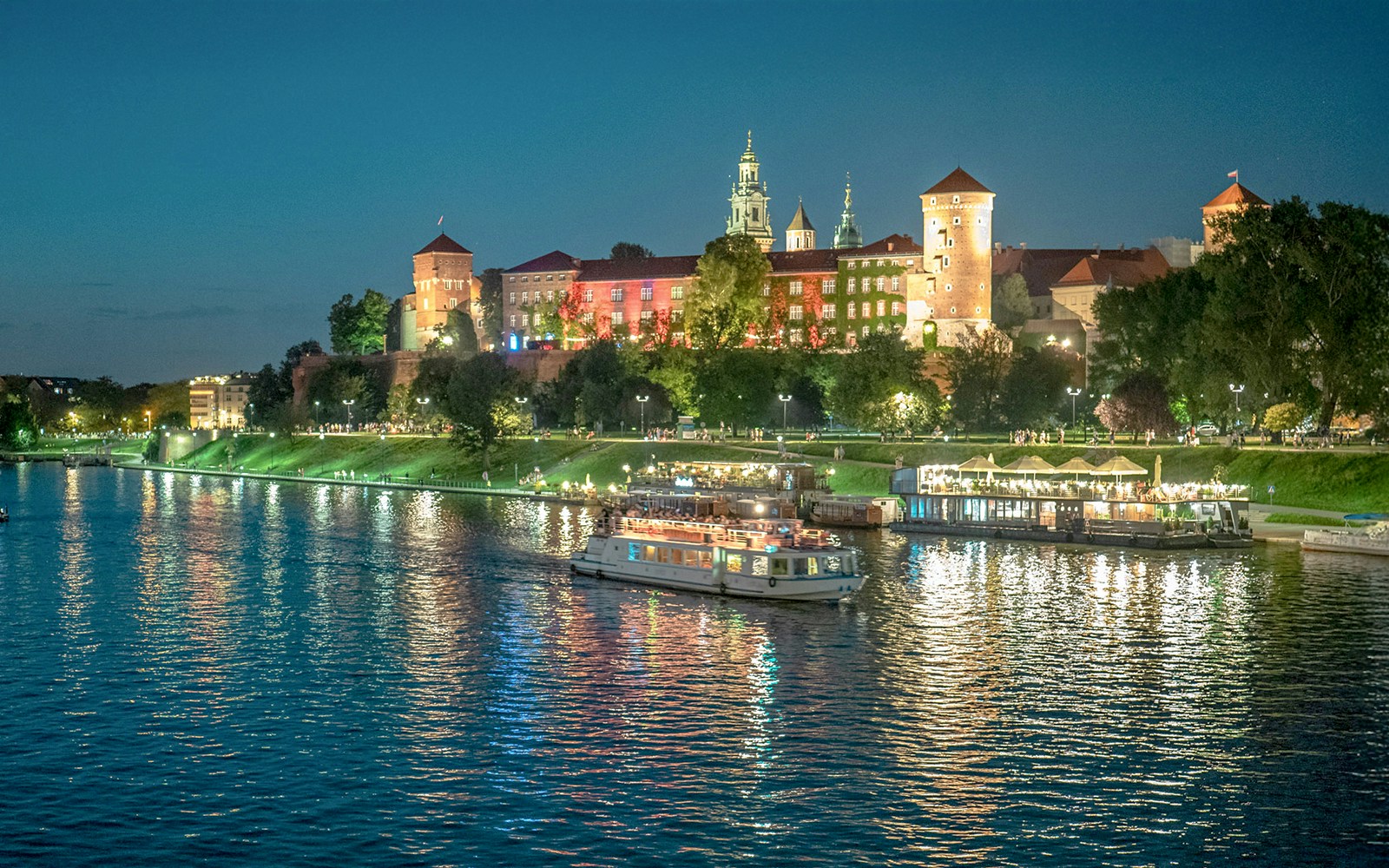 Vistula River cruise boat with tourists enjoying Krakow cityscape views.