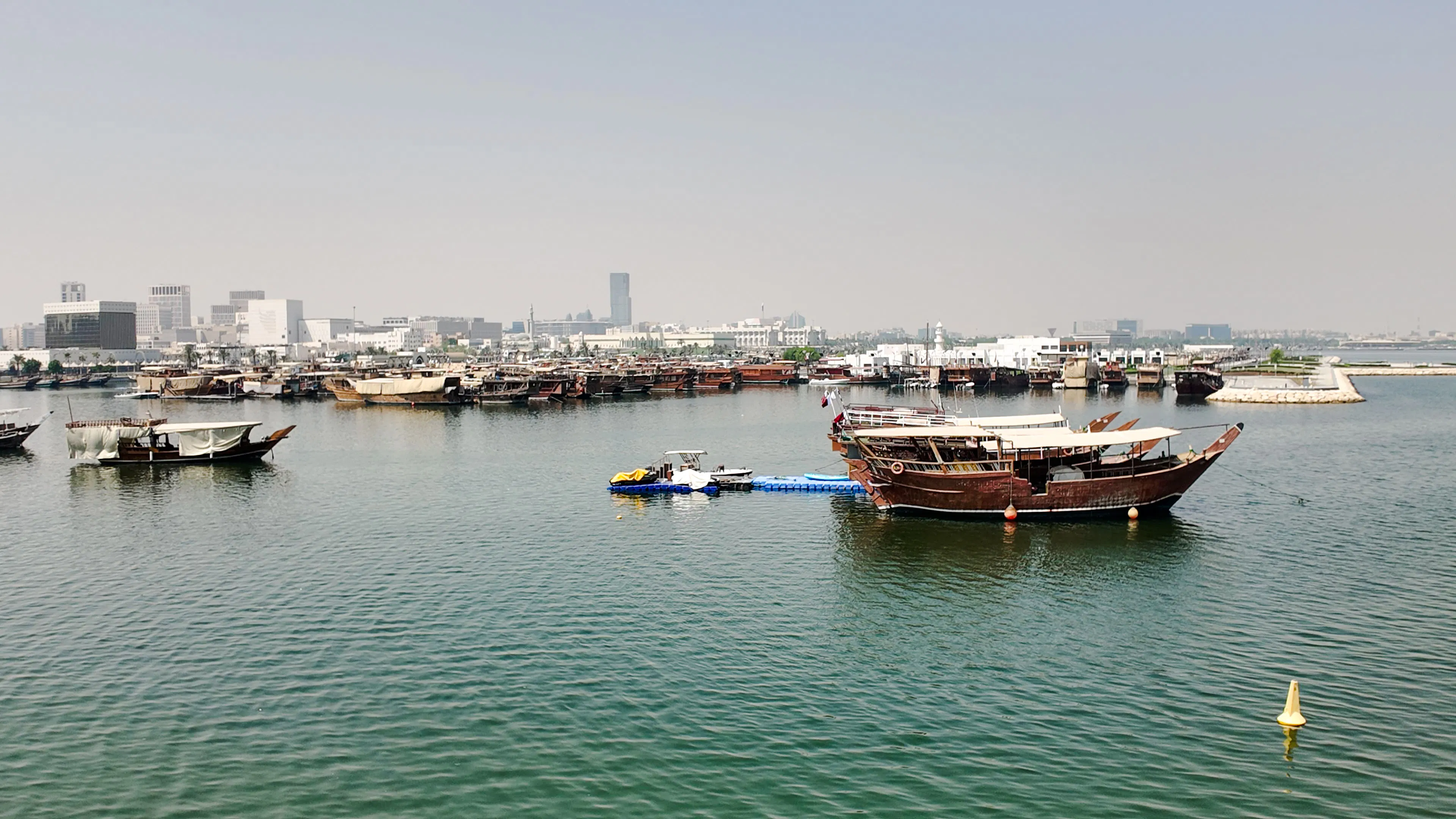 Traditional wooden boats in Doha harbor with city skyline in the background.