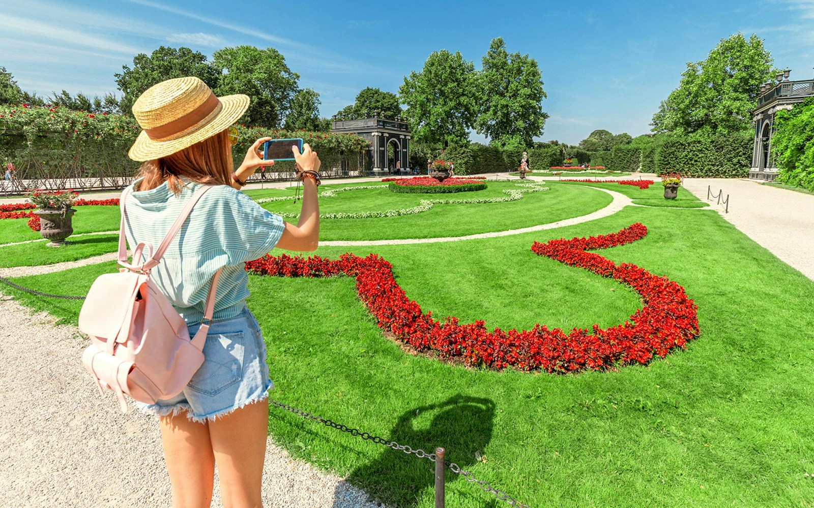 Tourist taking photo of Schönbrunn Palace Gardens, Vienna, with vibrant flower beds.