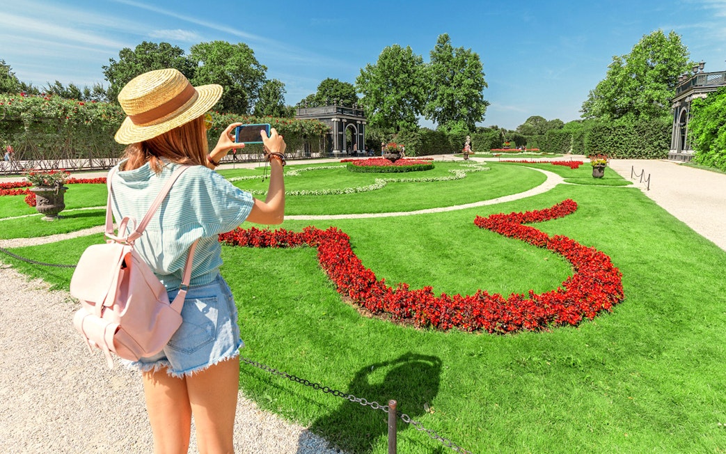 Tourist taking photo of Schönbrunn Palace Gardens, Vienna, with vibrant flower beds.