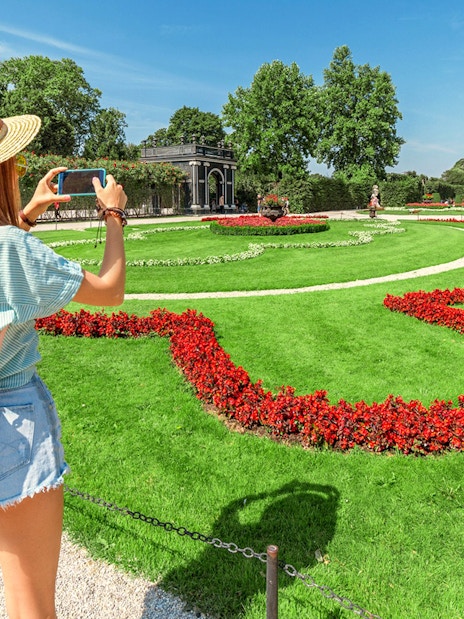 Tourist taking photo of Schönbrunn Palace Gardens, Vienna, with vibrant flower beds.