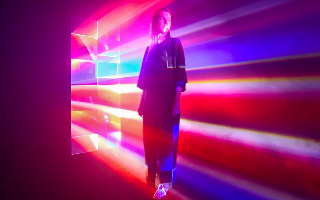 Guest surrounded by colorful light beams inside Light Art Museum exhibit.