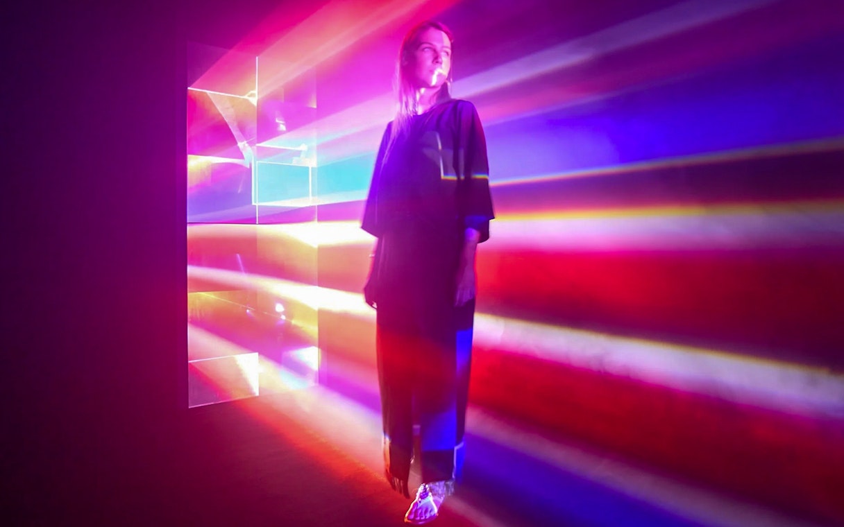 Guest surrounded by colorful light beams inside Light Art Museum exhibit.