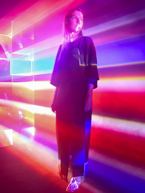 Guest surrounded by colorful light beams inside Light Art Museum exhibit.