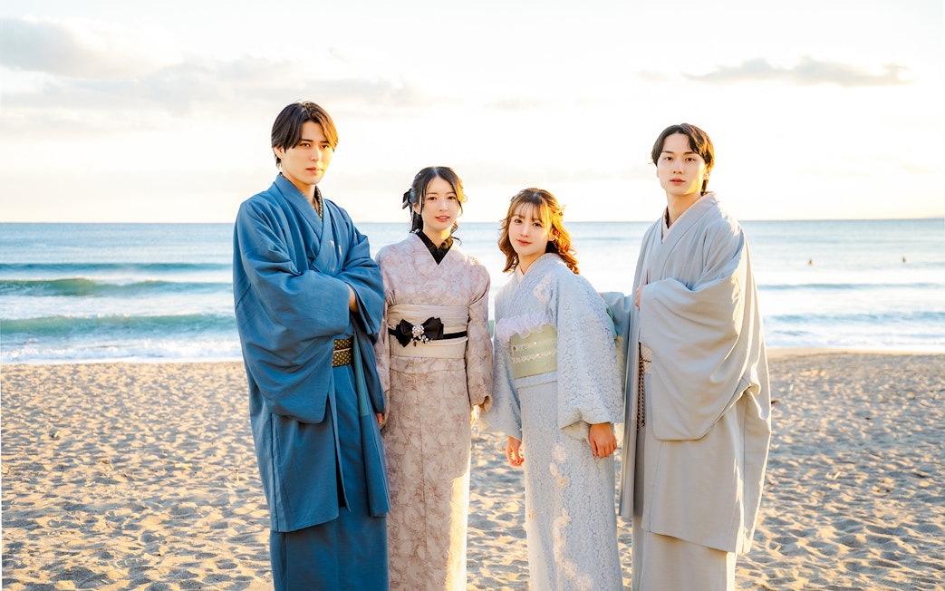 Tourists in kimono standing on a beach with ocean in the background.