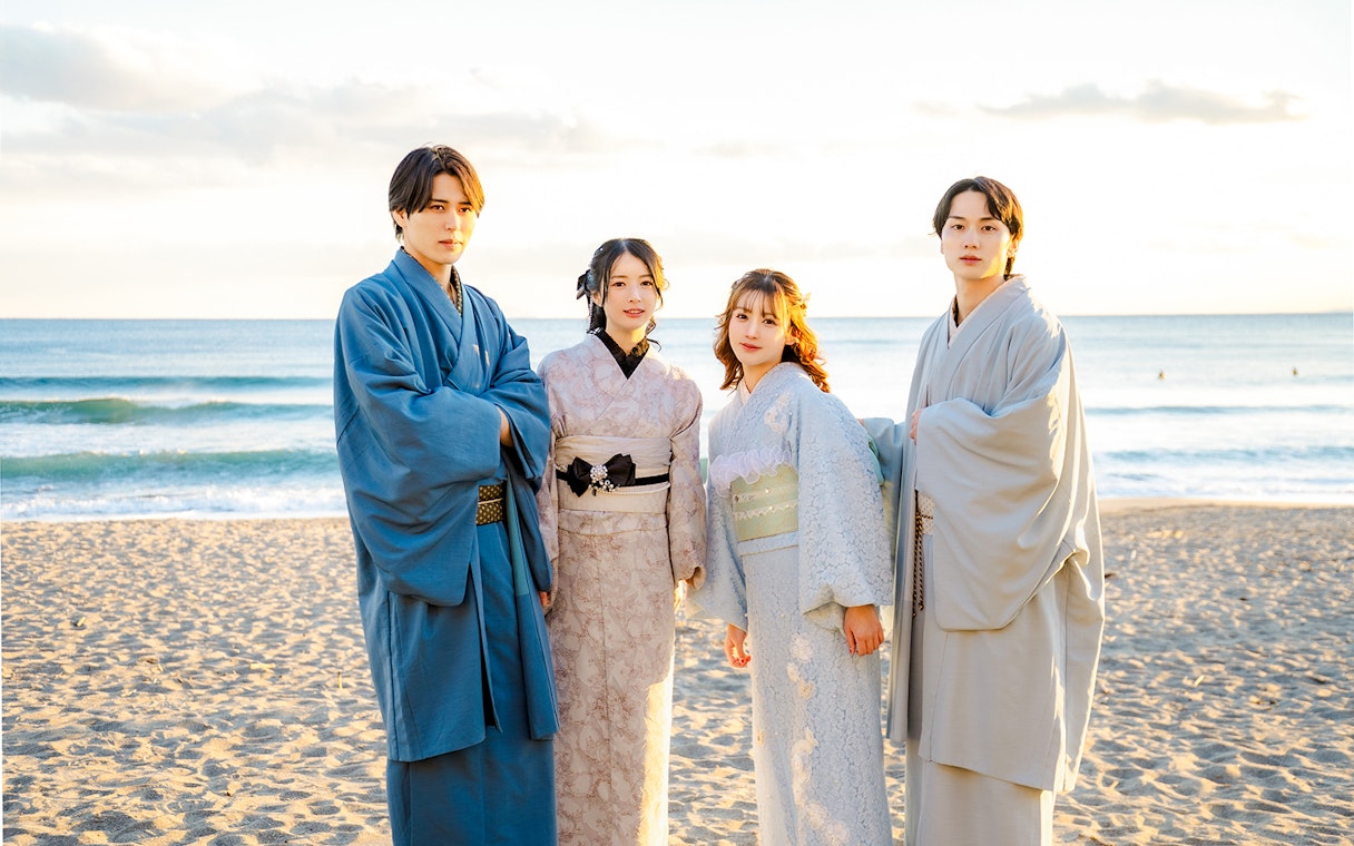 Tourists in kimono standing on a beach with ocean in the background.
