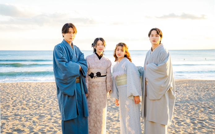 Tourists in kimono standing on a beach with ocean in the background.