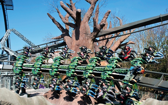 Roller coaster ride with passengers at Gardaland Park, Italy, featuring a large tree structure.