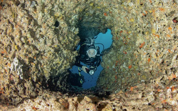 Diver exploring underwater cave during Scuba Diving Baptism in the Bosa Sea.