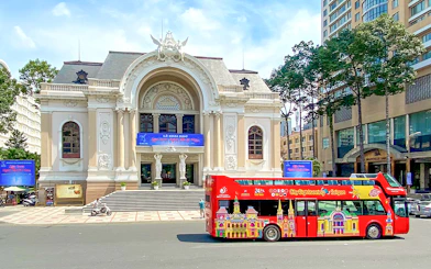 Red double-decker bus in front of Saigon Opera House on Hop-On Hop-Off tour.