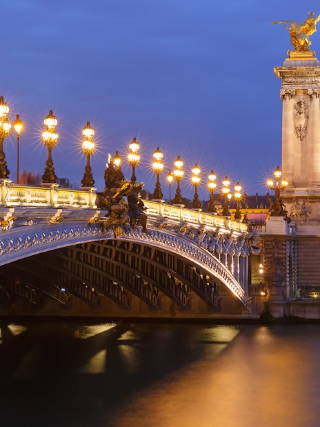 Night view of Pont Alexandre III and Les Invalides along the Seine in Paris, France.