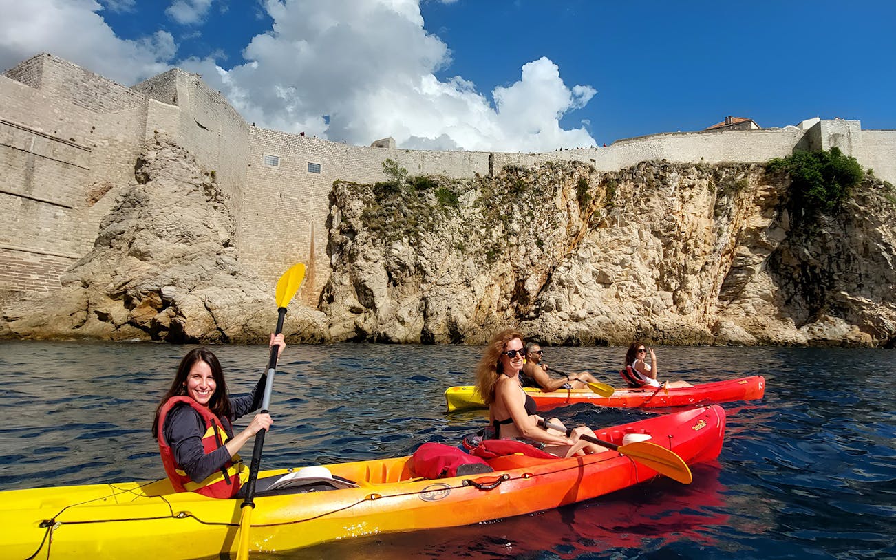 Kayakers near Betina Cave Beach with historic stone walls in the background.