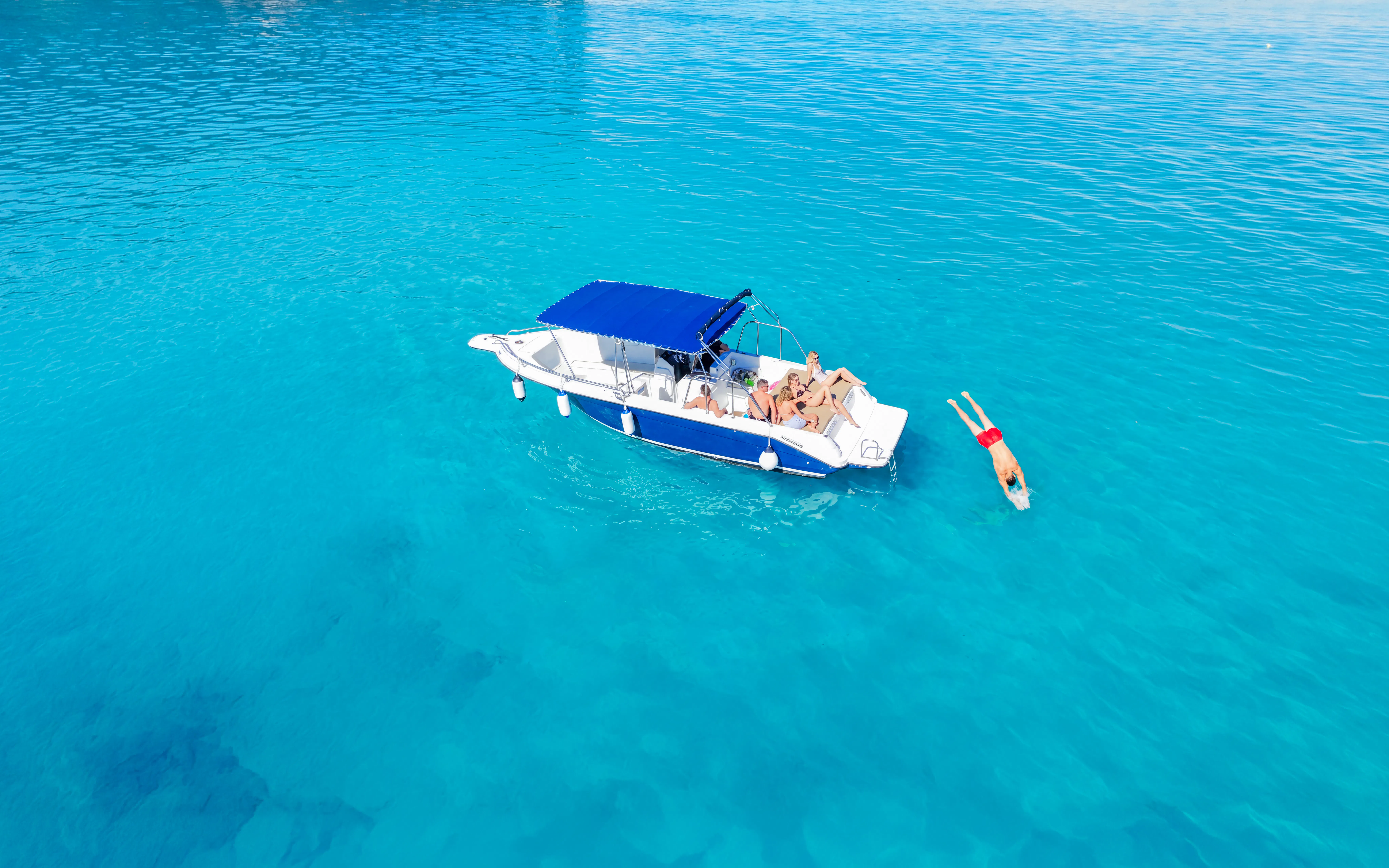 Boat with tourists in clear blue water near Cape Kamenjak, Croatia, with a person diving.
