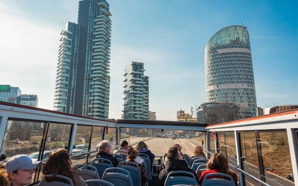 Open-top bus tour in Milan with modern skyscrapers in the background.