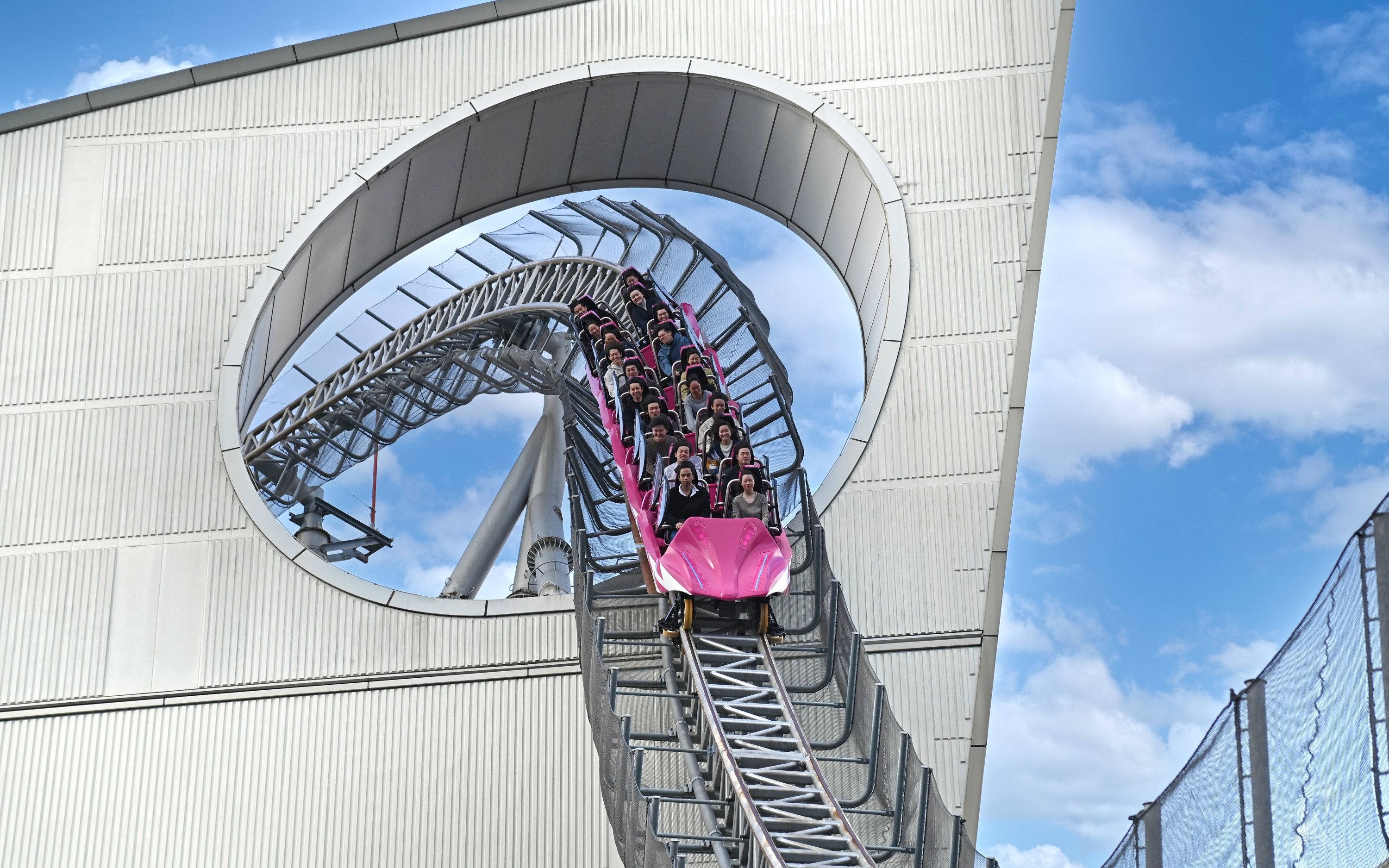 Roller coaster descending through a building loop near Tokyo Dome.