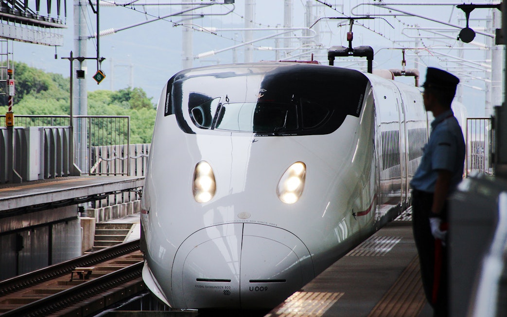 Bullet train arriving at Japanese station platform with station master nearby.