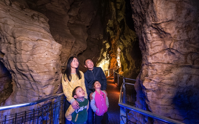 Family exploring illuminated Aranui Cave on guided tour, New Zealand.
