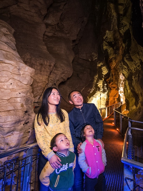 Family exploring illuminated Aranui Cave on guided tour, New Zealand.