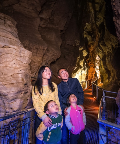 Family exploring illuminated Aranui Cave on guided tour, New Zealand.
