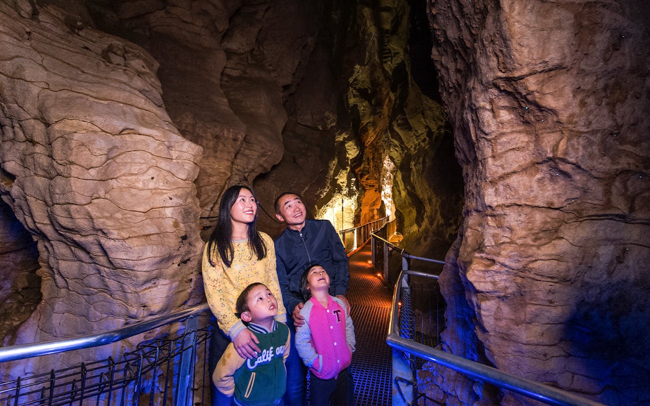 Family exploring illuminated Aranui Cave on guided tour, New Zealand.