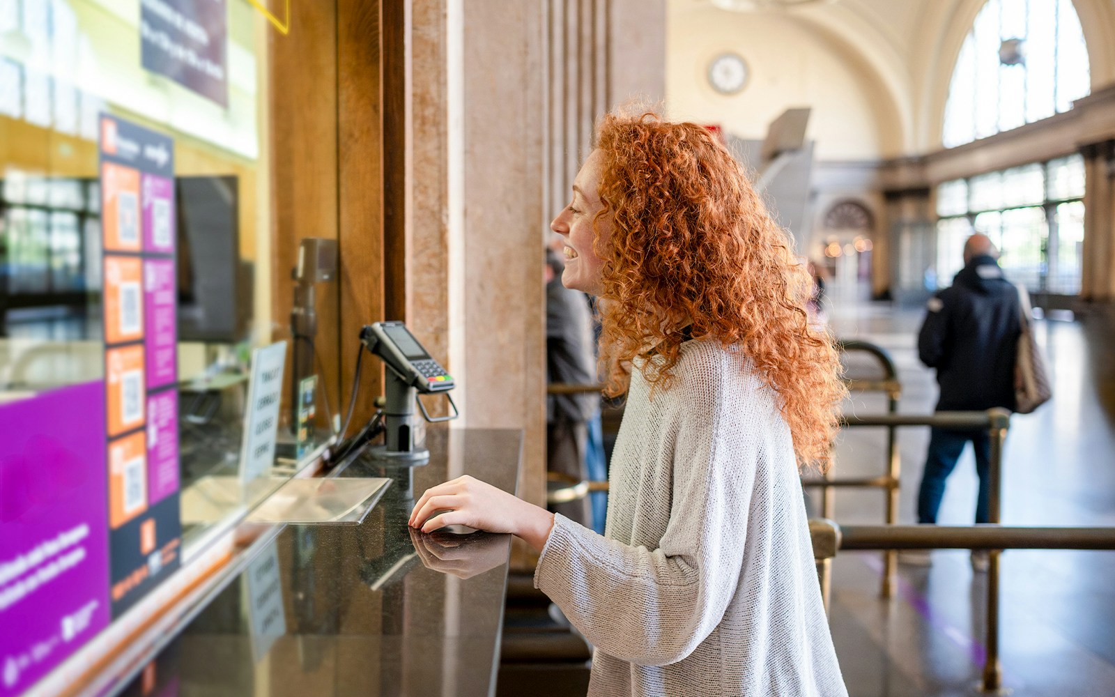 Young woman purchasing ticket at a station counter.
