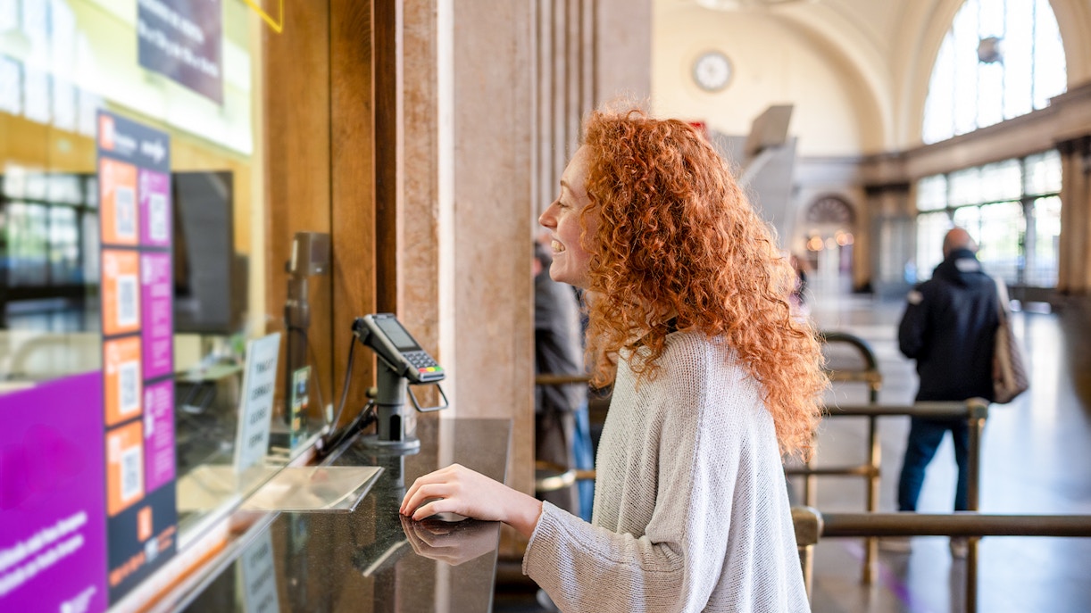 Young woman purchasing ticket at a station counter.