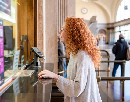 Young woman purchasing ticket at a station counter.