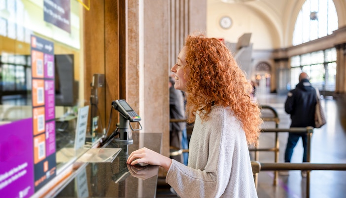 Young woman purchasing ticket at a station counter.