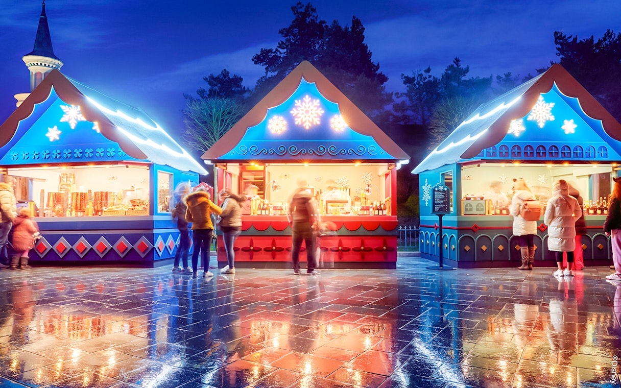 Christmas market stalls at Disneyland Paris 2025 with festive lights and visitors.