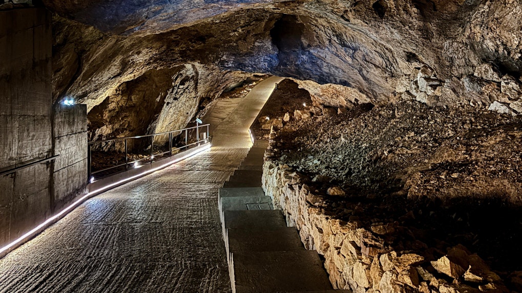 Pathway inside Lipa Cave, Montenegro with illuminated rocky walls and ceiling.