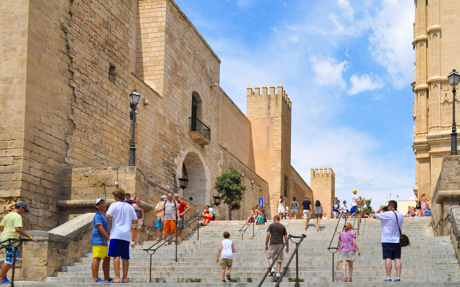 Visitors walking up stone steps towards historic walls in PalmaBus excursion, Palma de Mallorca.