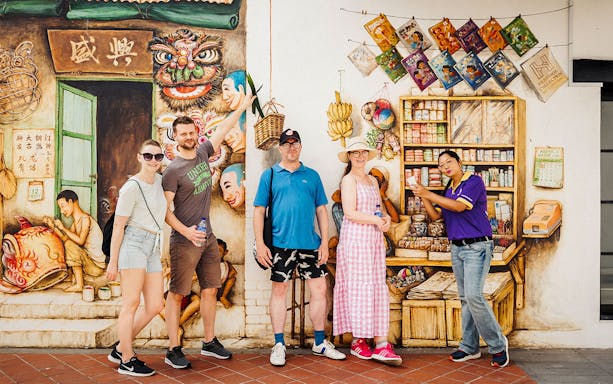 Tourists posing in front of a colorful mural during a guided Michelin and local hawker food tour.